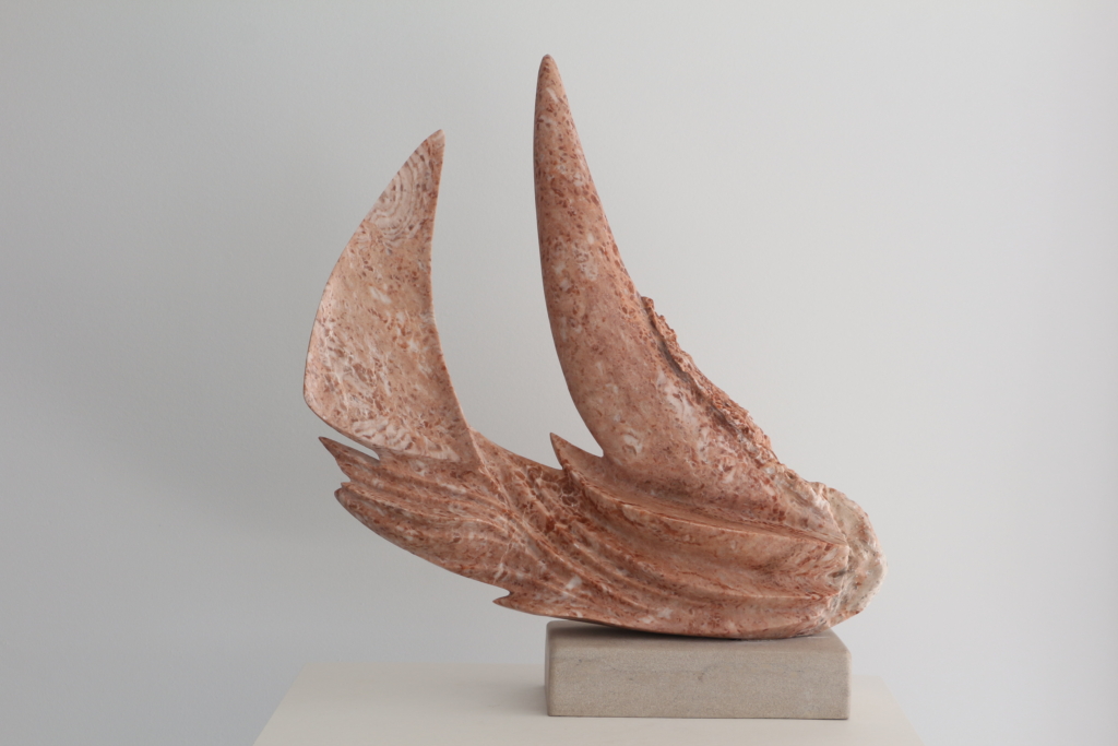 Sculpture abstraite en pierre rose veinée de terre cuite, en forme de voiles ou d'ailes courbées, posée sur une base en pierre beige.