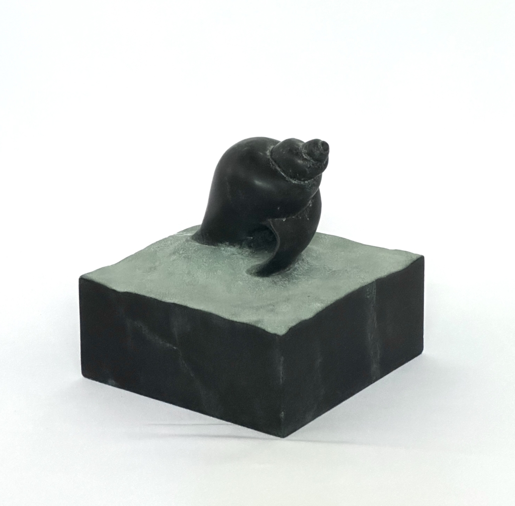 Petite sculpture en pierre sombre représentant une conque, posée sur une base en pierre grise.