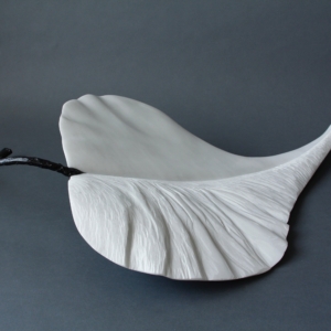 Sculpture en marbre blanc en forme de feuille, avec une tige noire évoquant une brindille.