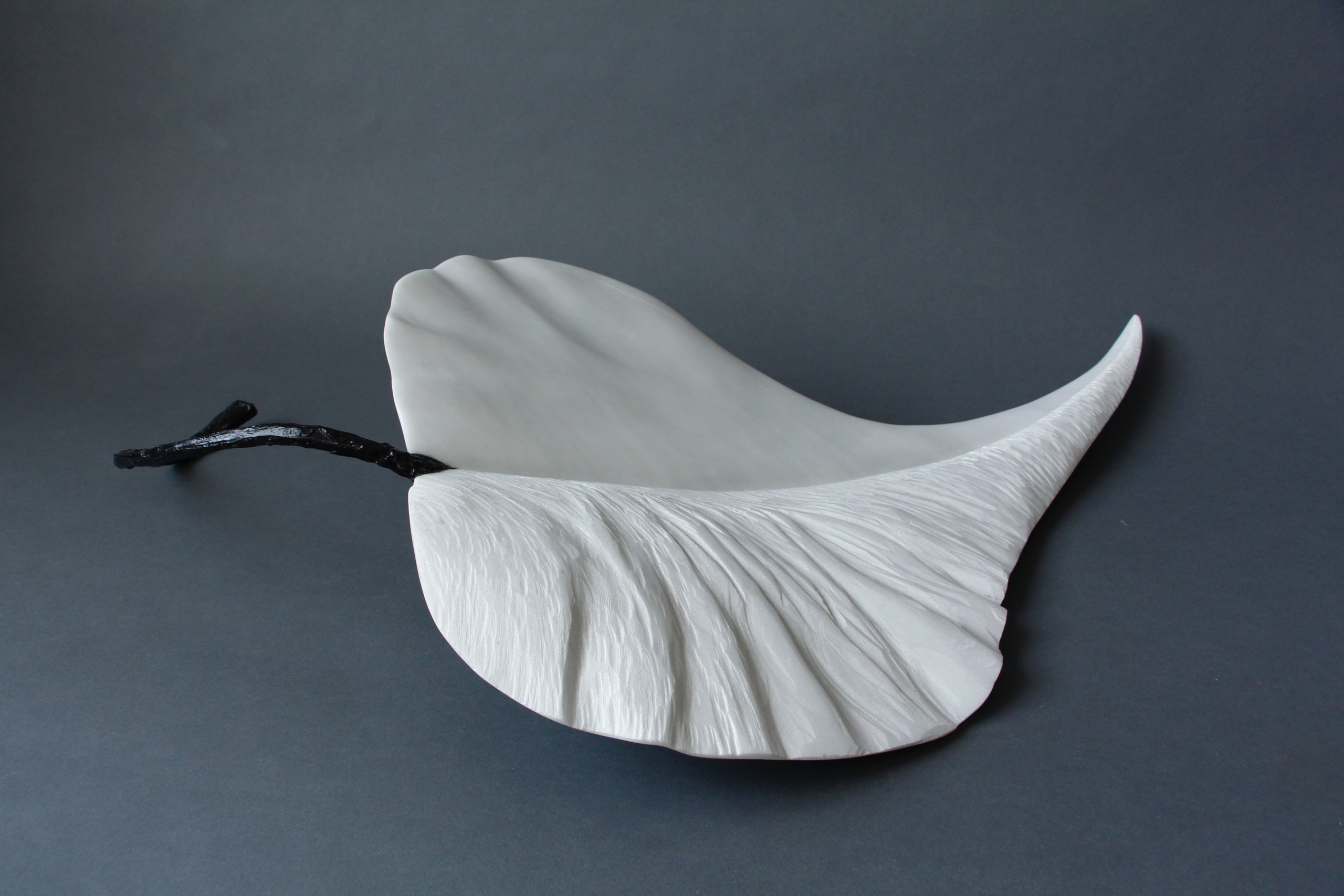 Sculpture en marbre blanc en forme de feuille, avec une tige noire évoquant une brindille.